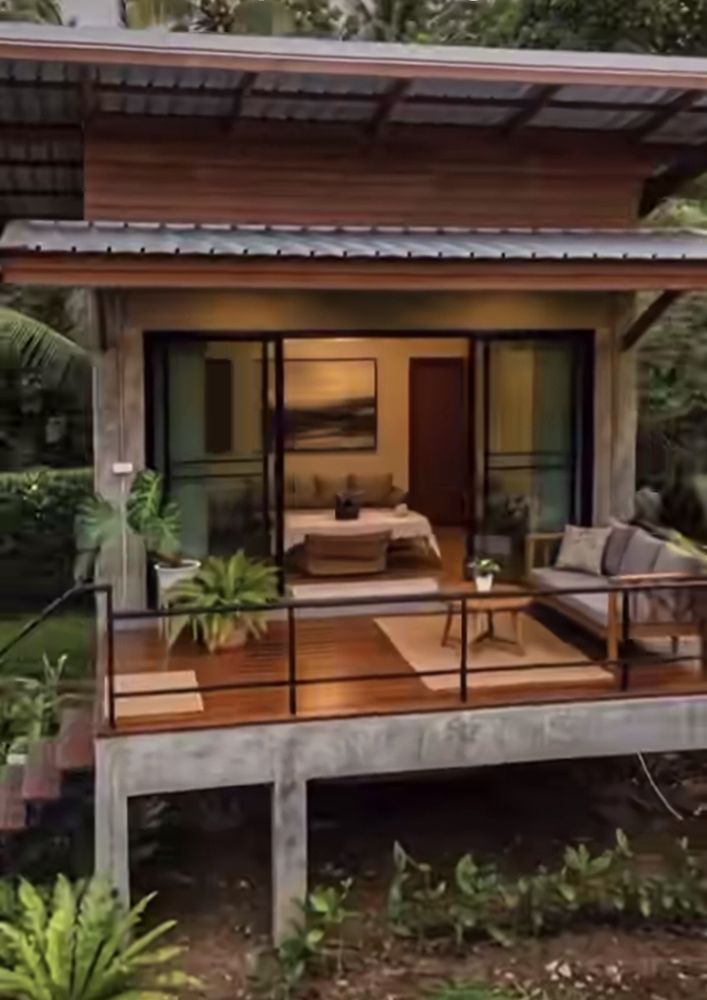 Casa con terraza de madera y salón iluminado entre vegetación